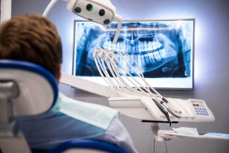 Person in dental chair looking at screen showing x ray of teeth