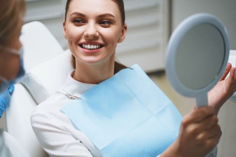 Woman in dental chair holding a mirror while talking to her dentist