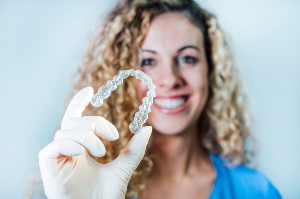 Invisalign in Melrose | Dentist holding clear aligners.