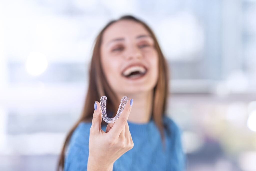 Smiling woman in dental chair holding an Invisalign clear aligner