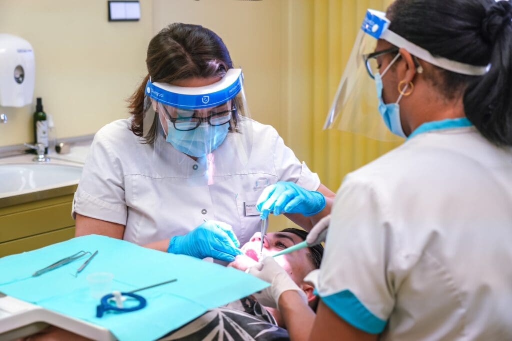 A person receiving dental treatment with two dentists working together, using various tools.