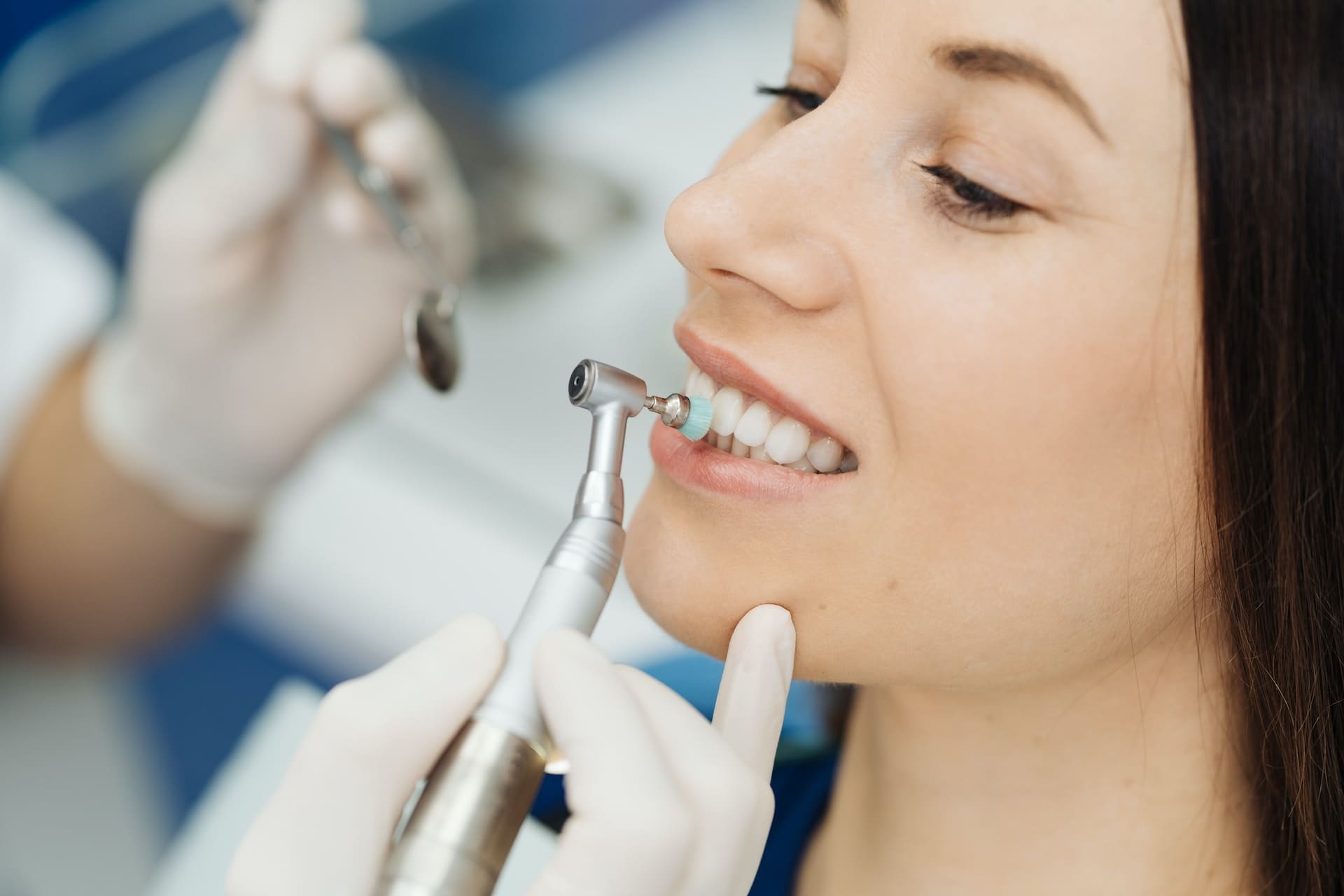 A girl sitting in a dental chair while a dentist applies porcelain veneers to her teeth.