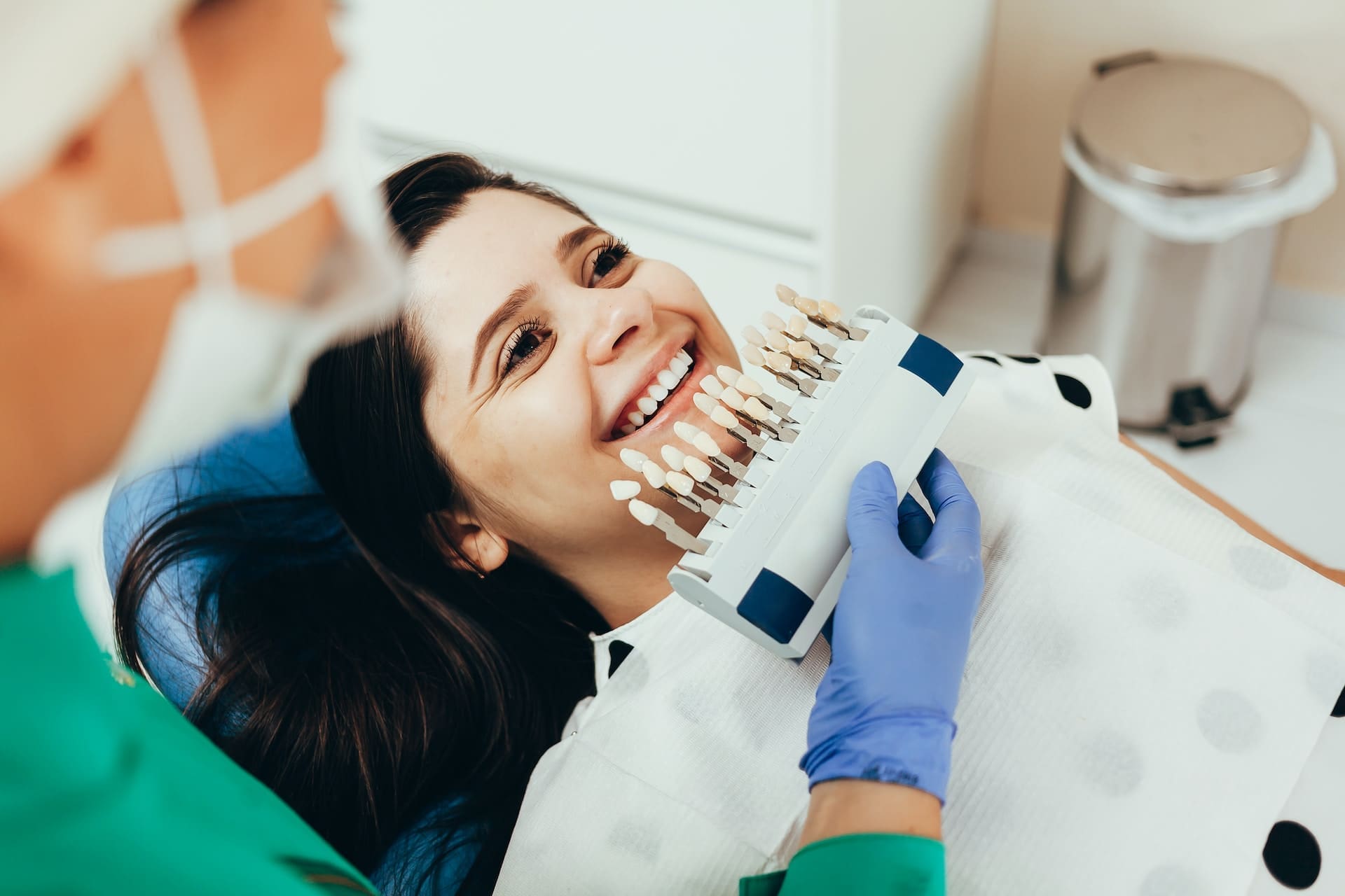 Cosmetic dentist holding a shade guide next to a patient smiling in the dental chair