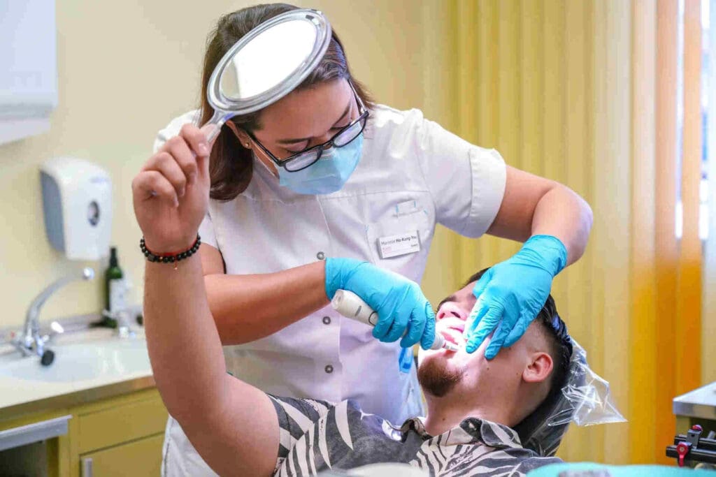 Dental patient holding a mirror while his dentist performs a treatment on him