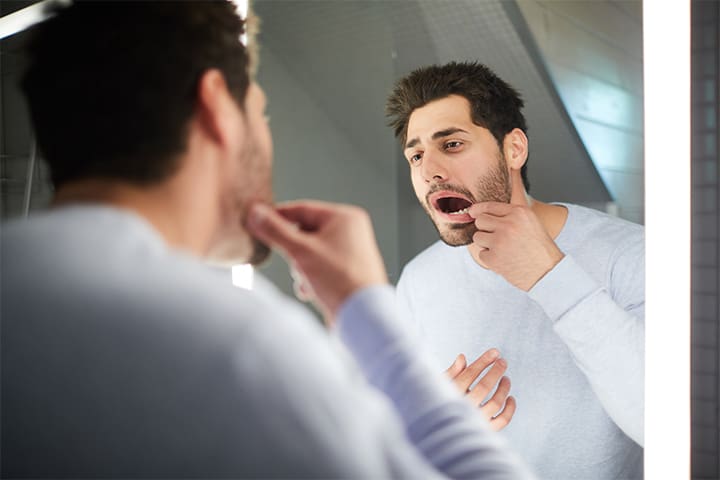 A man inspecting his tooth in a mirror.