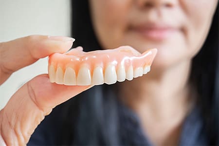 A woman holding an upper denture between her fingers