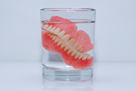 Dentures soaking in a glass of water.