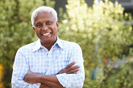 Senior man smiling outside with his arms folded.