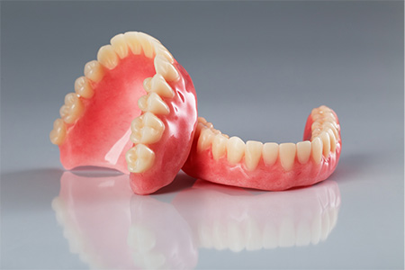 Two full dentures sitting on a reflective surface.