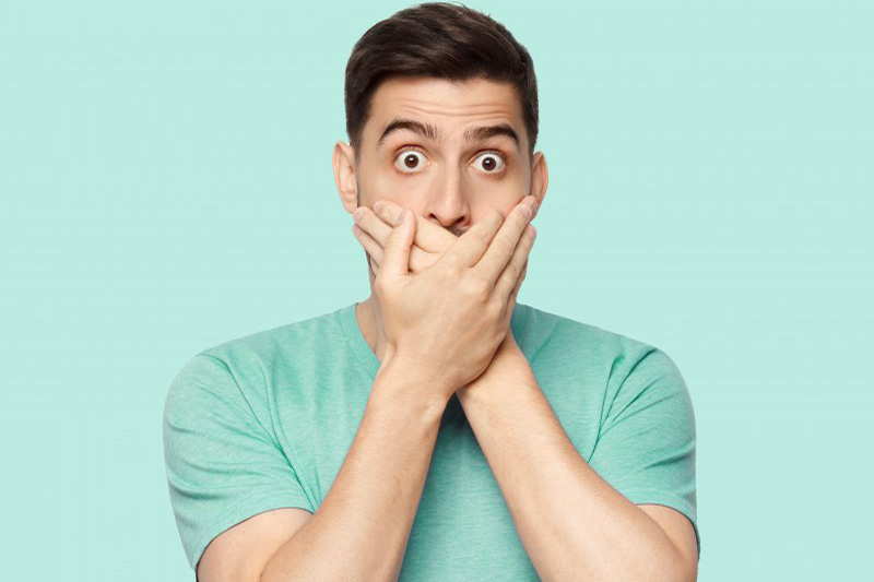 Man covering his mouth after his filling fell out.
