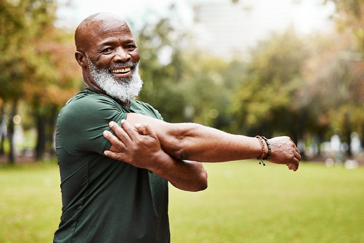 Bearded man smiling and stretching outside.
