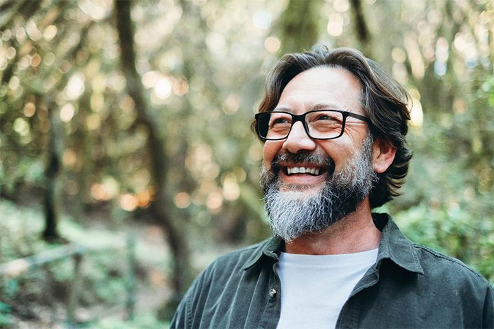 Man with glasses and beard smiling outdoors.