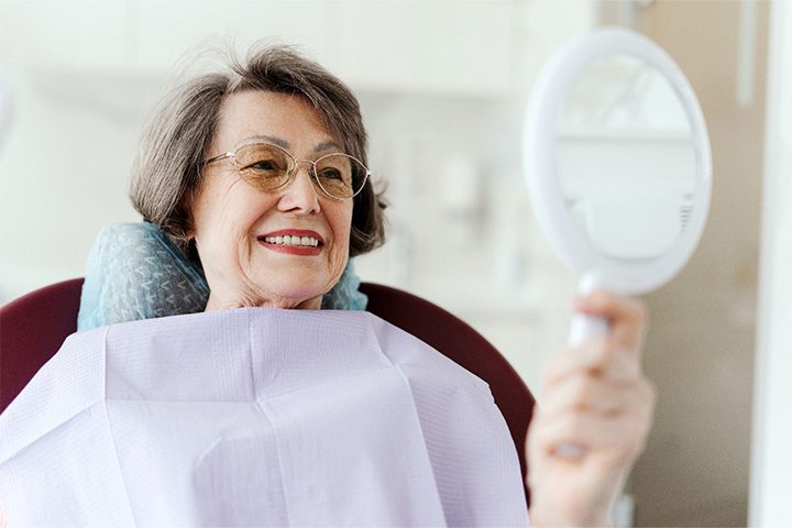 Senior woman checking smile in mirror.